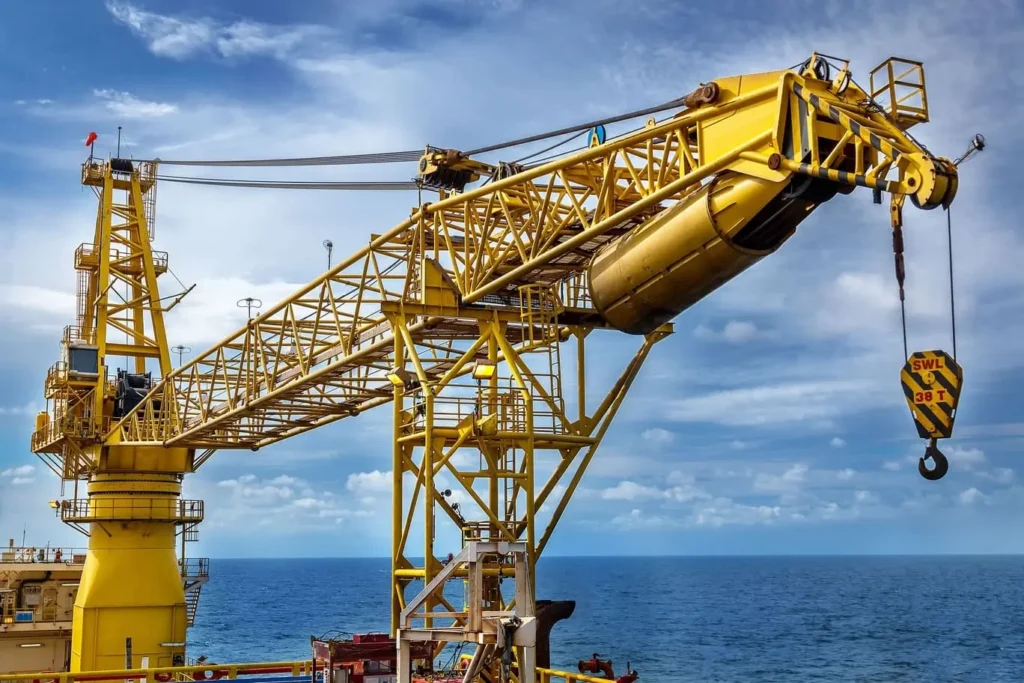 A large yellow industrial crane stands on an offshore platform against a backdrop of ocean and a partly cloudy sky, portraying a landscape of maritime industry.