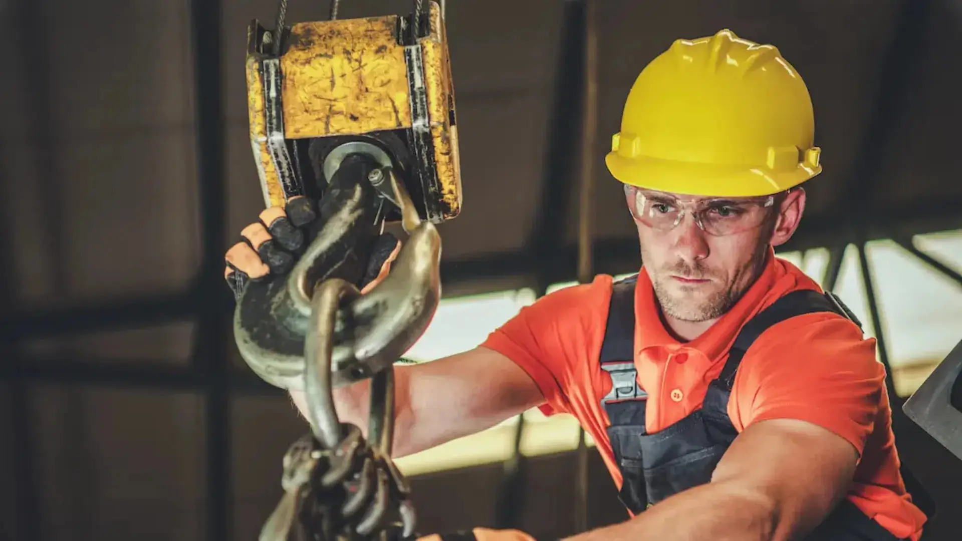 A construction worker wearing a yellow hard hat and protective glasses carefully operates a large hook with a focused expression, highlighting safety and concentration during Rigger Level 1 Training.